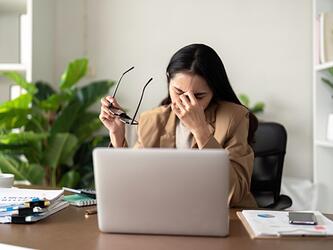stressed woman sitting in front of laptop at desk surrounded by paper and notes